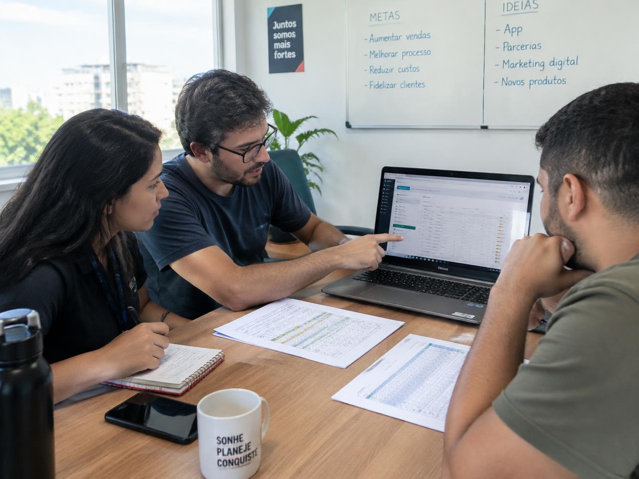 Pequena equipe analisando planilhas e um sistema de gestão no notebook